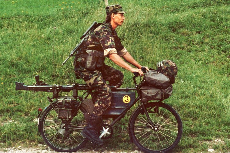 Ein Soldat, ausgerüstet mit Waffen und Gepäck, fährt mit einem der neuen Dienstfahrräder der Schweizer Armee. Aufgenommen am 21. Juli 1991.